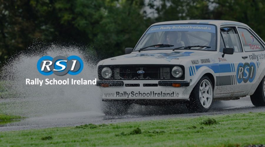 A rally car with "Rally School Ireland" branding drives on a wet road, spraying water as it passes by, an exhilarating sight that makes you think of the thrilling tours and activities one could experience.